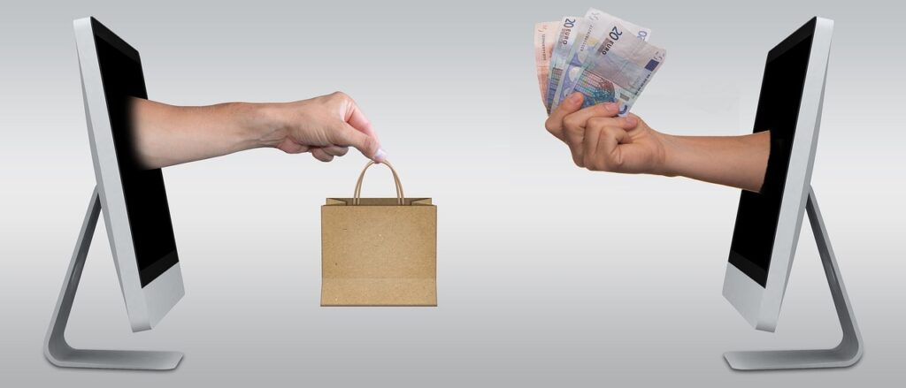 A hand with a shopping bag going through a computer screen to reach the computer screen that is accrues from it with a hand that has money.