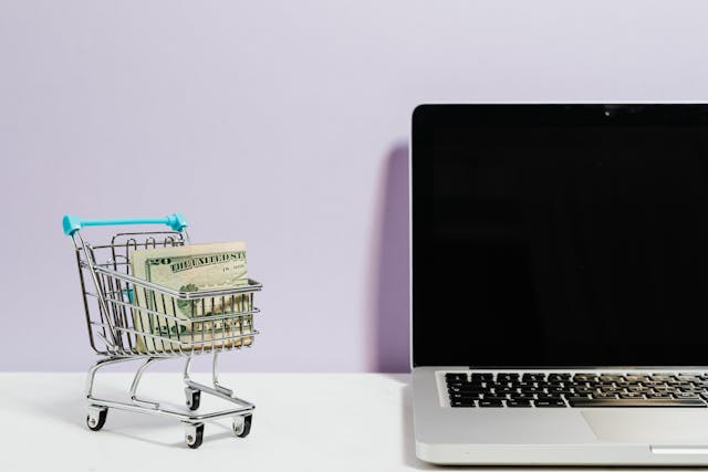 Miniature cart filled with a $20 bill next to a Macbook. Couponing service.