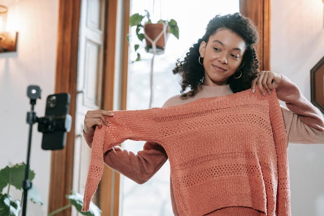 A woman showing off a peach colored sweater, presumably having affiliate links.