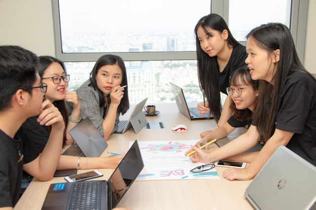 Group of people with computers drafting marketing plan onto paper.