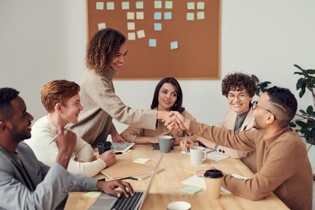 Room of interns smiling while woman shakes hand with man.