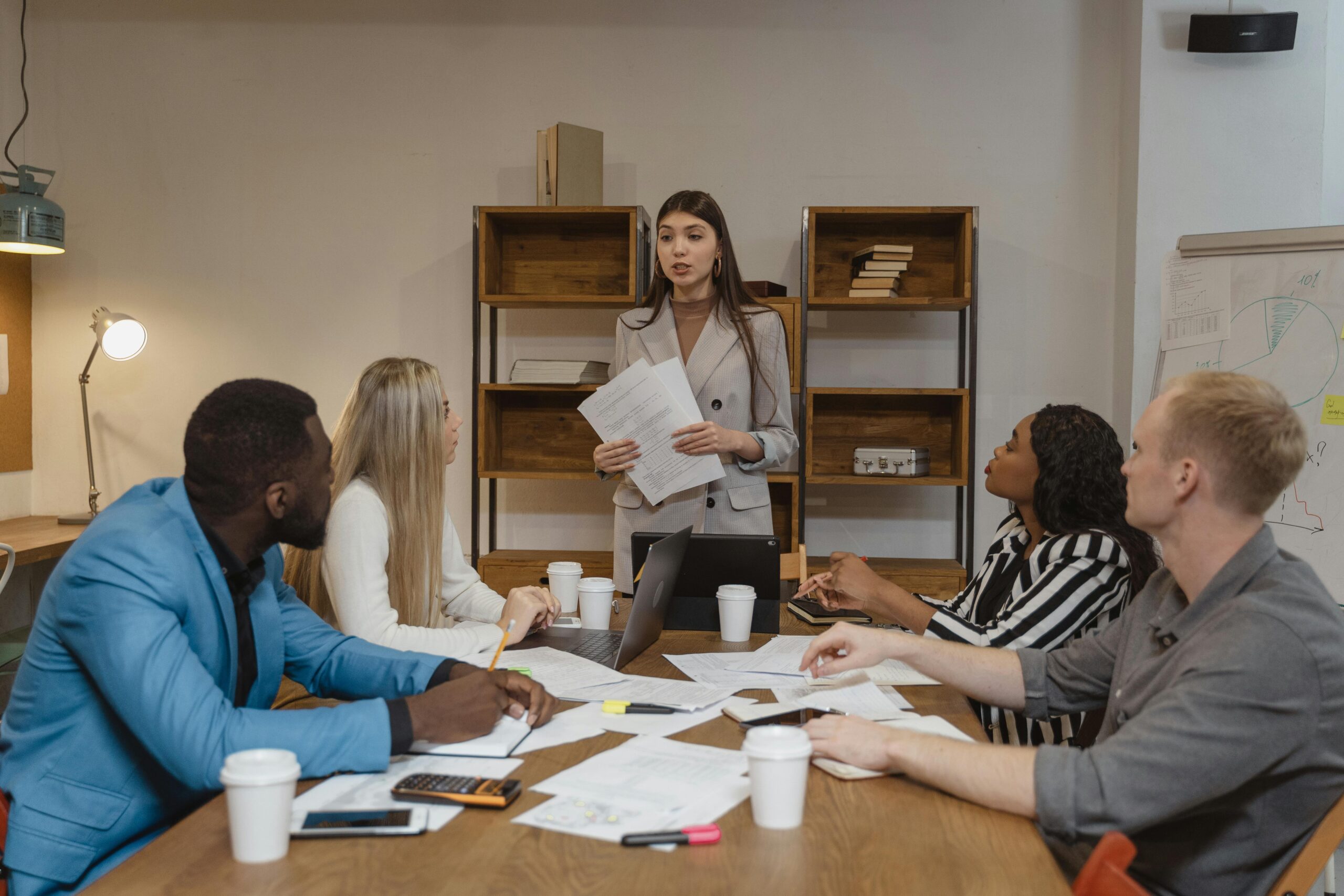 A woman standing and presenting a report to four people sitting at the office table