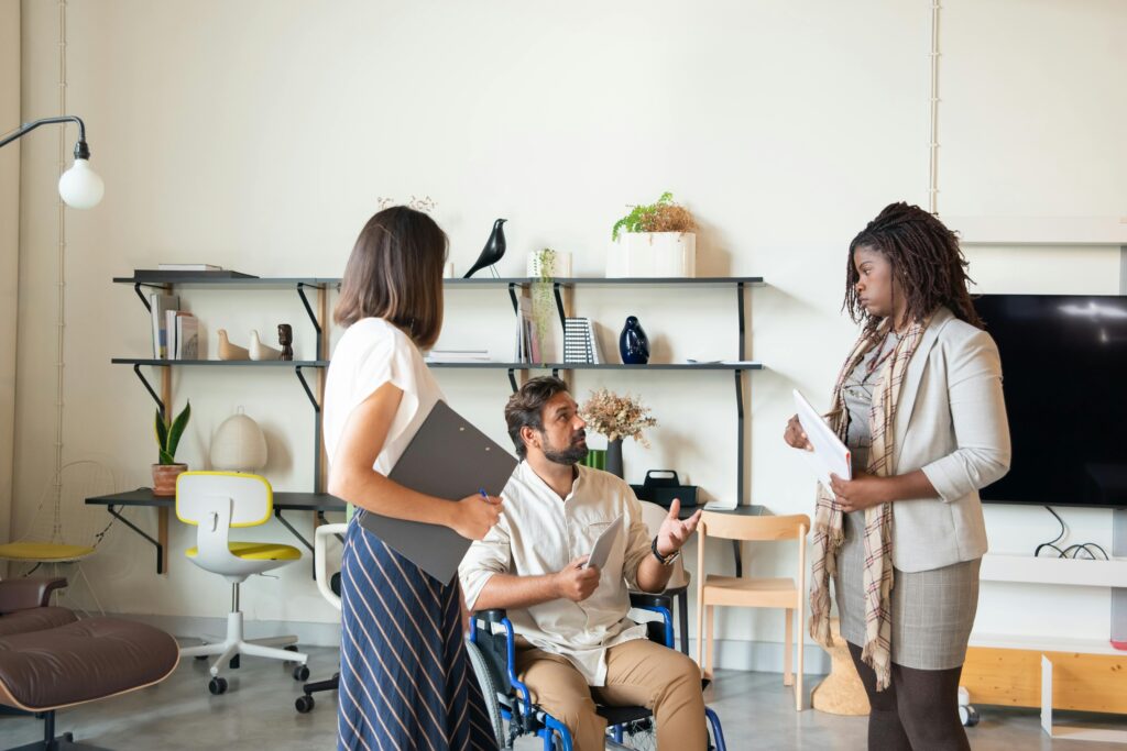 A man sitting on his wheelchair while talking to two women who are standing