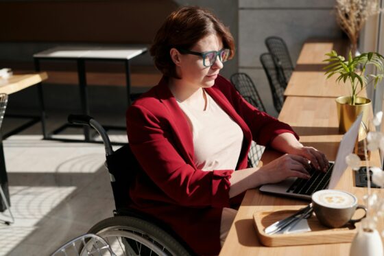 A woman sitting on a wheelchair and typing on a laptop